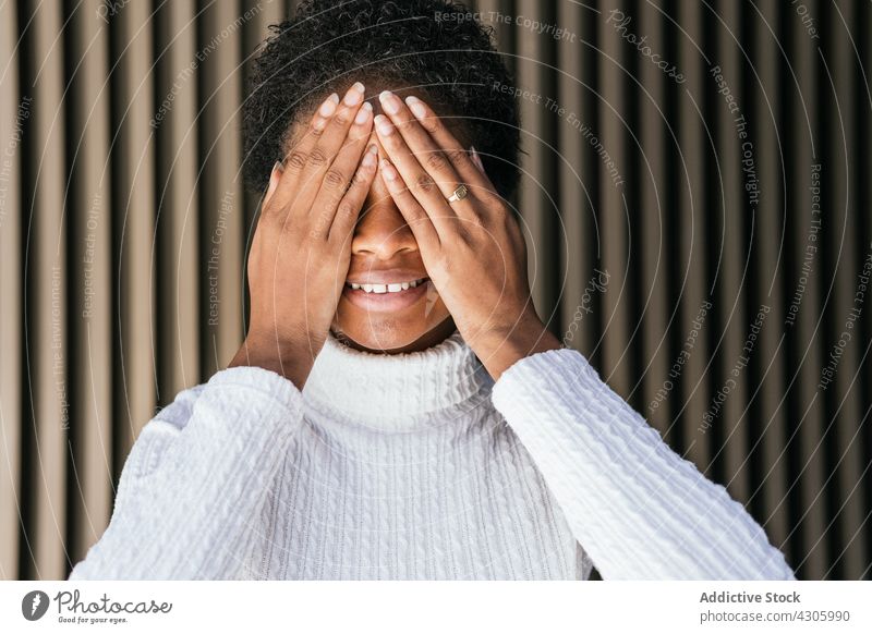 Fröhliche schwarze Frau bedeckt Auge Lächeln Auge abdecken Glück Stil urban Straße Großstadt Outfit Mode Afroamerikaner ethnisch jung Ohrringe sorgenfrei