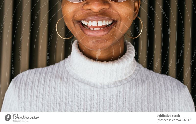 Crop schwarze Frau fröhlich lächelnd Lächeln Stil Straße urban modern Wand Glück Mode Pullover Ohrringe Accessoire Freude lückenhafte Zähne Afroamerikaner