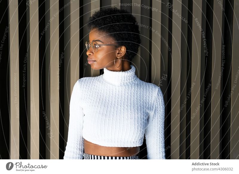 Junge Afroamerikanerin in der Nähe einer gestreiften Hauswand Frau Lächeln Glück Stil urban Straße Großstadt Outfit Mode schwarz ethnisch jung Ohrringe