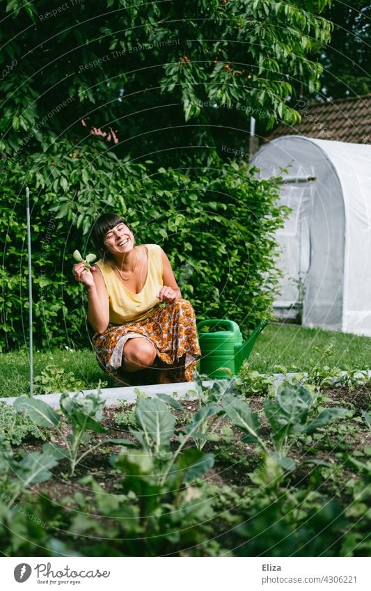 Frau sitzt im Garten vor einem Gemüsebeet und freut sich über ein selbst geerntetes Radieschen Beet ernten Gartenarbeit Beete Nutzpflanze Pflanze Gemüsegarten