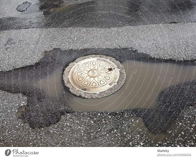 Schön verzierter runder Kanaldeckel mit großer Pfütze im Sonnenschein nach einem Regenschauer in Adapazari in der Provinz Sakarya in der Türkei Deckel Gully