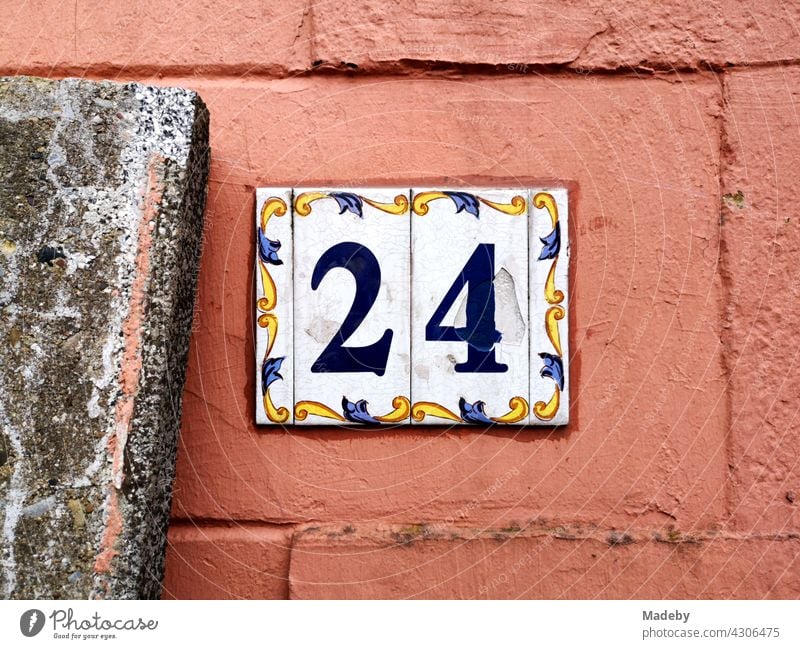 Hausnummer 24 als Schild aus Emaille mit Verzierung und Ornament auf alter Fassade in Orange in Oerlinghausen bei Bielefeld im Teutoburger Wald in Ostwestfalen-Lippe