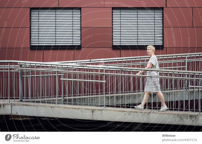 Eine Frau in einem gestreiften Kleid läuft durch eine urbane Welt voller Streifen Linien Passantin Jalousien Fassade Fenster Stadt geschlossen Aufgang Rampe