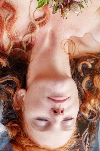 Gorgeous Porträt einer jungen sexy Frau Ophelia mit lockigen roten Haaren liegen mit Blumen mit geschlossenen Augen sterben im Wasser in den See Braut ophelia