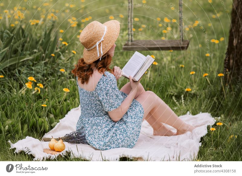 Frau mit Buch auf Picknickdecke in der Natur ruhend lesen Sommer Roman Strohhut Wiese Decke sich[Akk] entspannen Landschaft Gras Wochenende Kleid Etage Freizeit