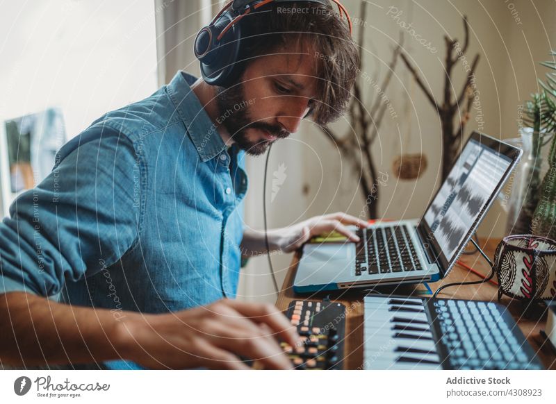 Musiker mit Synthesizer und Laptop zu Hause benutzend heimwärts Kopfhörer Mann jung Tisch Atelier Gerät Apparatur Spieler Aufnahme Raum Appartement Freizeit