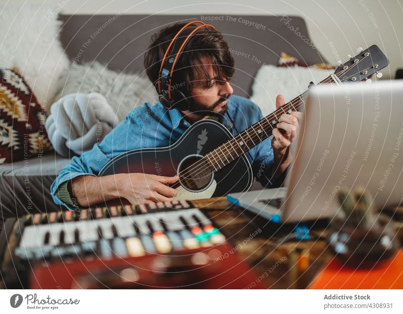 Musiker spielt auf der Gitarre in der Nähe des Laptops zu Hause heimwärts Spielen Kopfhörer Mann jung Tisch Synthesizer Atelier Gerät Apparatur Instrument