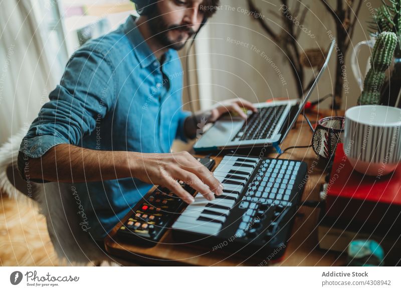 Musiker mit Synthesizer und Laptop zu Hause benutzend heimwärts Kopfhörer Mann jung Tisch Atelier Gerät Apparatur Spieler Aufnahme Raum Appartement Freizeit