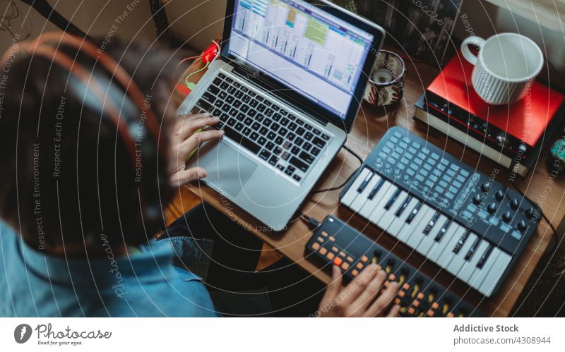 Anonymer Musiker mit Synthesizer und Laptop zu Hause benutzend heimwärts Kopfhörer Mann jung Tisch Atelier Gerät Apparatur Spieler Aufnahme Raum Appartement