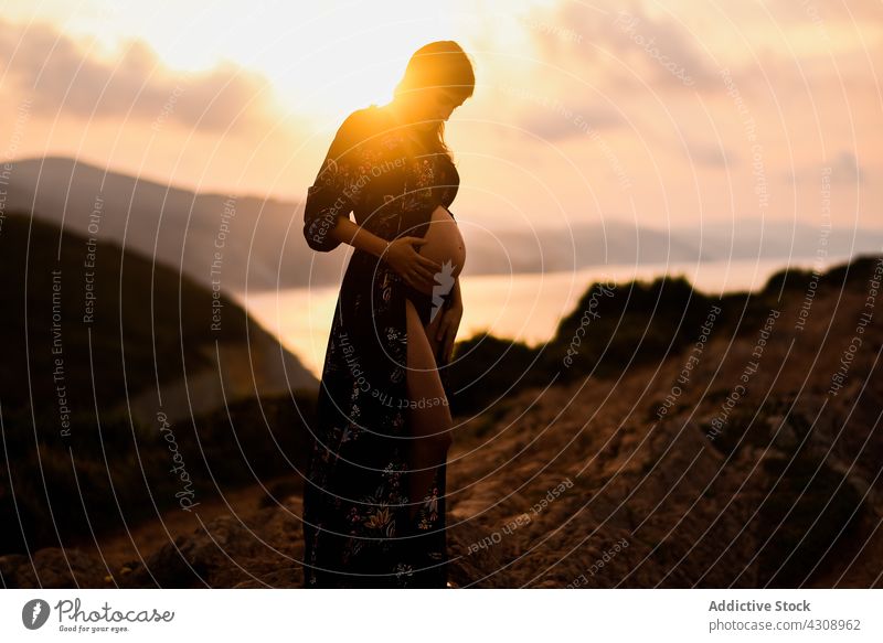 Schwangere Frau steht auf einem Hügel bei Sonnenuntergang schwanger Silhouette Berge u. Gebirge friedlich erwarten Natur Mutter träumen Bauch mütterlich