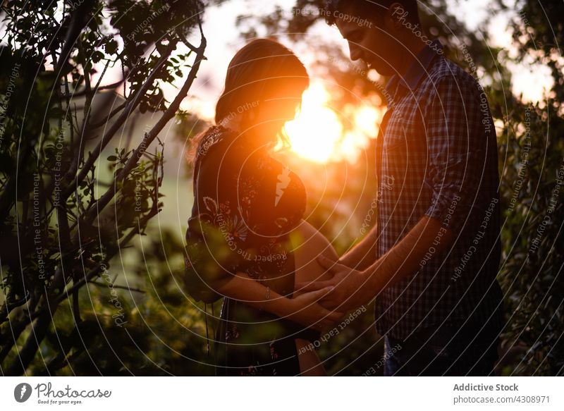 Liebender Mann berührt den Bauch einer schwangeren Frau im Licht des Sonnenuntergangs Paar Zusammensein Glück Natur Partnerschaft erwarten romantisch Zuneigung