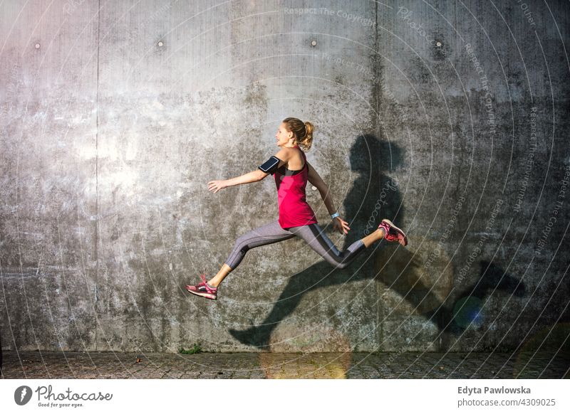 Junge Frau springt gegen graue Wand springend Aktion Gesundheit Tanzen Übung Flexibilität Jogger Läufer Joggen rennen Menschen jung Energie Bekleidung