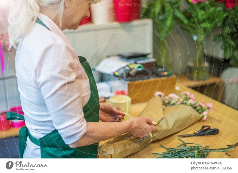 Frau arbeitet im Blumenladen Blumenhändler Haufen Blumenstrauß Beteiligung Menschen Erwachsener Senior reif schön attraktiv Lächeln Glück Schürze Mitarbeiter