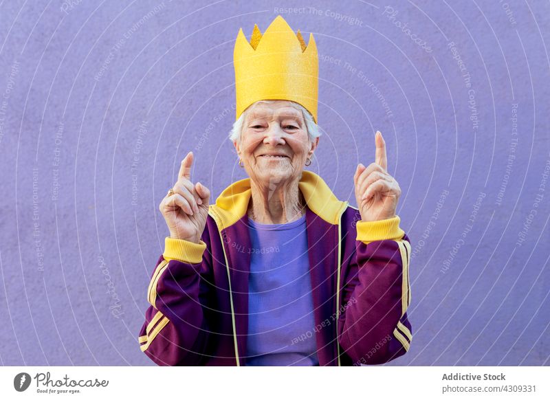 Lächelnde ältere Sportlerin mit dekorativer Krone und erhobenen Fingern mit dem Finger nach oben zeigen Königin achtsam freundlich Konzept Porträt Frau
