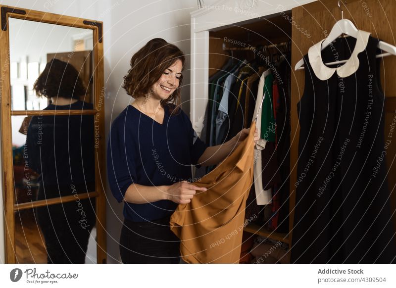 Fröhliche Frau bei der Auswahl von Kleidungsstücken aus dem Kleiderschrank wählen Bekleidung Outfit heimwärts Lächeln Glück Kleiderbügel untersuchen Erwachsener