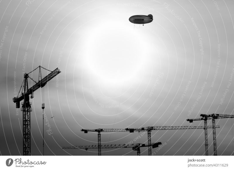 Zeppelin über Baukräne Sonne Gegenlicht Himmel Baukran Silhouette Schwarzweißfoto Baustelle Sonnenlicht fliegen Kurs Schönes Wetter Kontrast Hintergrund neutral