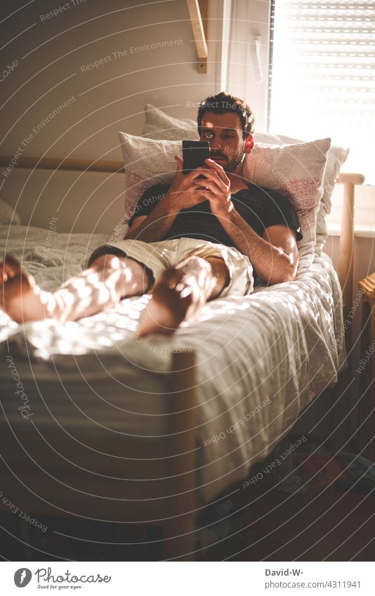 Mann mit Handy in den Händen im Bett lesen chillen Nachrichten Telekommunikation Smartphone Kommunizieren Lifestyle Technik & Technologie ausruhen
