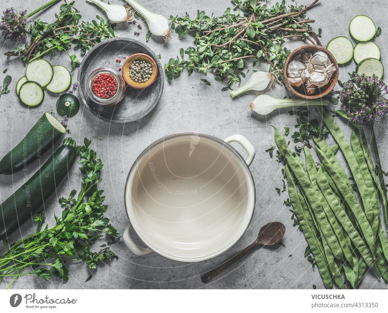 Verschiedene gesunde grüne Zutaten auf Betonküchentisch mit Gewürzen und weißem Kochtopf, Draufsicht. Veganes Essen verschiedene Gesundheit Küche Tisch
