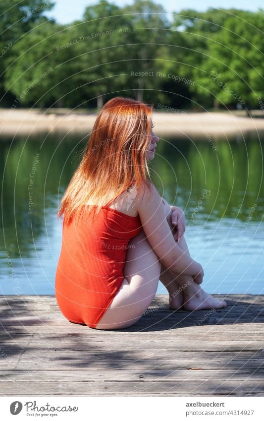 junge Frau in rotem Badeanzug sitzt auf Holzsteg am Badeteich Junge Frau Badesee Sommer Schwimmen & Baden Wasser See Ferien & Urlaub & Reisen Außenaufnahme