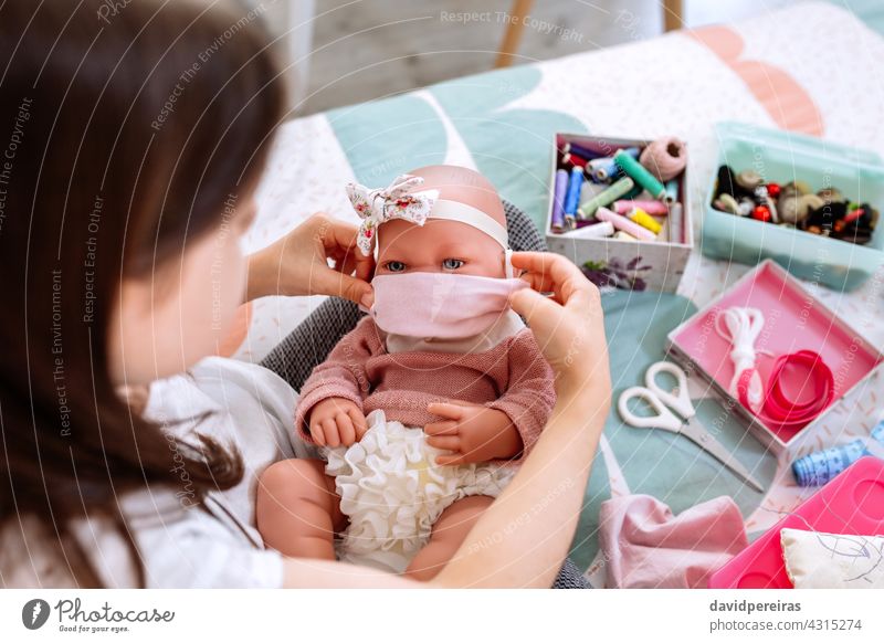 Mädchen probiert ihrer Puppe eine Maske an, die sie gerade näht Schutz Pflege Coronavirus Babypuppe Nähkästchen Maske aufsetzen Gesichtsmaske unkenntlich