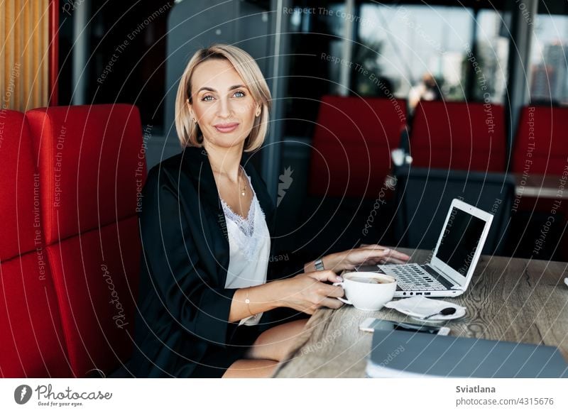 Ein schönes blondes Mädchen benutzt einen Laptop und arbeitet in einem Café. Pause, online arbeiten, freiberuflich benutzend Computer Arbeit Internet Business