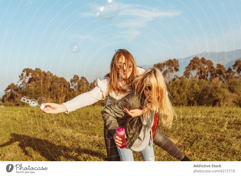 Glückliche Freundinnen reiten Huckepack und blasen Seifenblasen Frauen bester Freund Spaß Natur Zusammensein Lachen Freizeit Freundschaft Partnerschaft