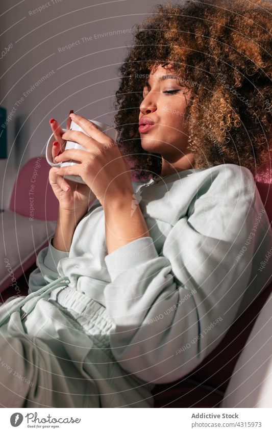 Schwarze Frau trinkt zu Hause Kaffee trinken heimwärts heiß Getränk genießen Tasse Afro-Look Frisur ethnisch Afroamerikaner schwarz Sofa Tee Liege krause Haare