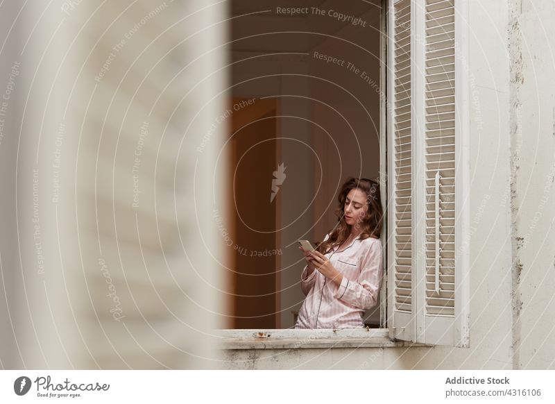Ruhige Frau, die in der Nähe des Fensters auf ihrem Smartphone surft Browsen zuschauend Pyjama Gespräch Morgen Mobile Telefon Telefonanruf Anruf Funktelefon