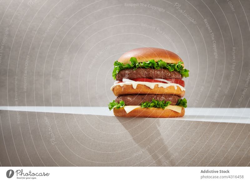 Appetitlicher Doppelburger auf grauem Hintergrund verdoppeln Burger Fastfood geschmackvoll Kotelett Junk Food lecker Käse Mahlzeit Brötchen Salat Lebensmittel