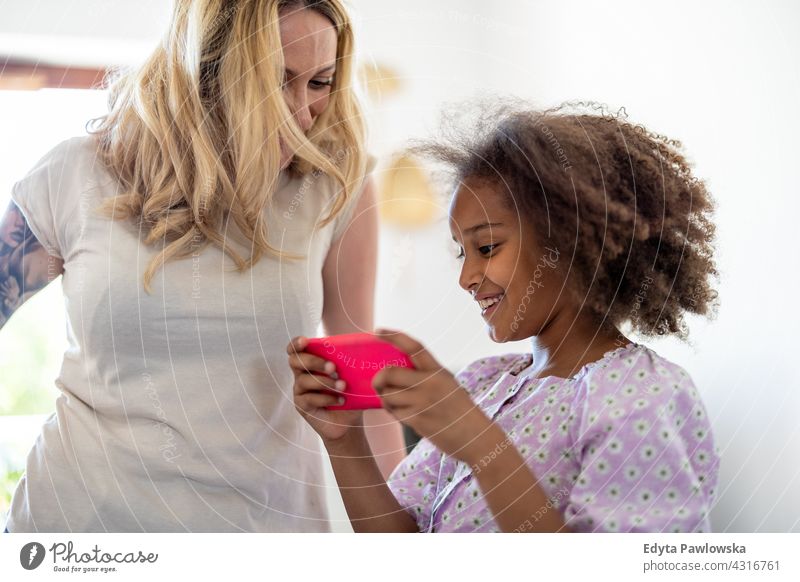 Junges Mädchen zeigt ihrer Mutter etwas auf einem Smartphone Kind Familie Tochter multiethnisch gemischte Rassenfamilie vielfältige Familie Vielfalt Afro-Look