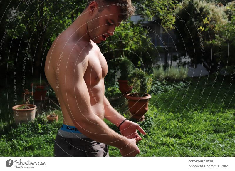 junger Mann lässt im Garten seine Muskeln spielen muskulös Körper Kraft Fitness Training Oberkörper Muskulatur attraktiv nackt Bodybuilding Stärke sportlich