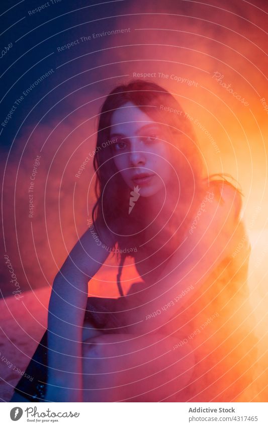 Junge Frau sitzt in Neonbeleuchtung Licht neonfarbig dunkel Projektor Model Stil Kunst Windstille allein jung sich[Akk] entspannen selbstbewusst besinnlich