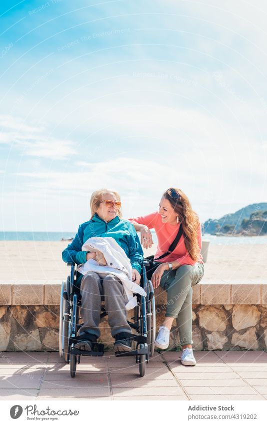 Tochter sitzt mit betagter Mutter im Rollstuhl an der Uferböschung älter Lächeln Stauanlage MEER deaktivieren sitzen Glück Zusammensein Handicap heiter