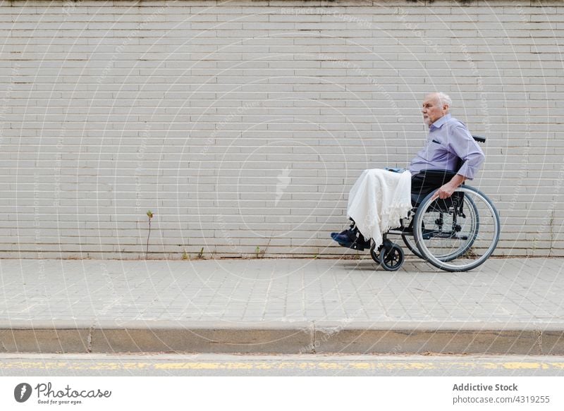 Älterer Mann im Rollstuhl auf der Straße Mitfahrgelegenheit Großstadt deaktivieren gealtert Senior Handicap älter männlich urban Straßenbelag Bürgersteig Stadt