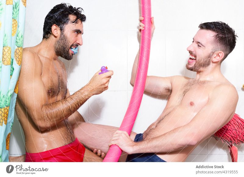 Verspieltes schwules Paar mit Spielzeug im Badezimmer Homosexualität Dusche Spaß haben lgbt Zusammensein Männer lustig spielen Liebe Partnerschaft multiethnisch