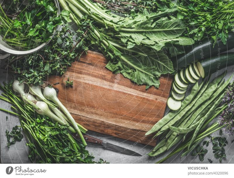 Lebensmittel Hintergrund mit einem Rahmen mit hölzernen Schneidebrett und verschiedene grüne Gemüse und Kräuter für leckere und gesunde Küche gemacht. Ansicht von oben.