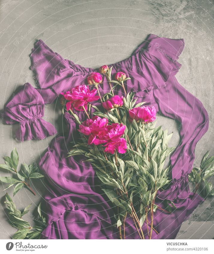 Lila Volantkleid mit Pfingstrosen Blumenstrauß . Mode und Schönheit flach legen. Kopieren Raum . Ansicht von oben purpur mit Volant Kleid Haufen