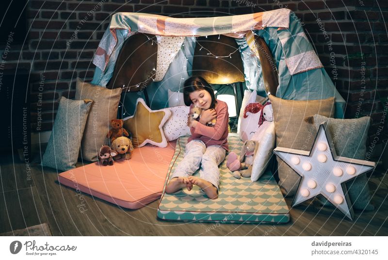 Mädchen umarmt ausgestopfte Puppe spielen in einem diy Zelt zu Hause lieblich geschlossene Augen umarmend kuscheln Plüschpuppe Lächeln süß charmant Kind