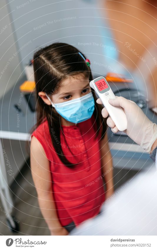 Mädchen mit Fieber, dessen Temperatur vom Arzt gemessen wird Infrarot-Thermometer Messung Symptom covid-19 Schutzmaske Kind krank kalt wenig digital Menschen