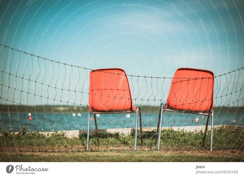 Zwei unbesetzte Stühle für Rettungsschwimmer am Seeufer Wasser Urlaub beobachten Absperrung blau orange Stuhl 2 leer Sitzgelegenheit Stapelstuhl Bojen
