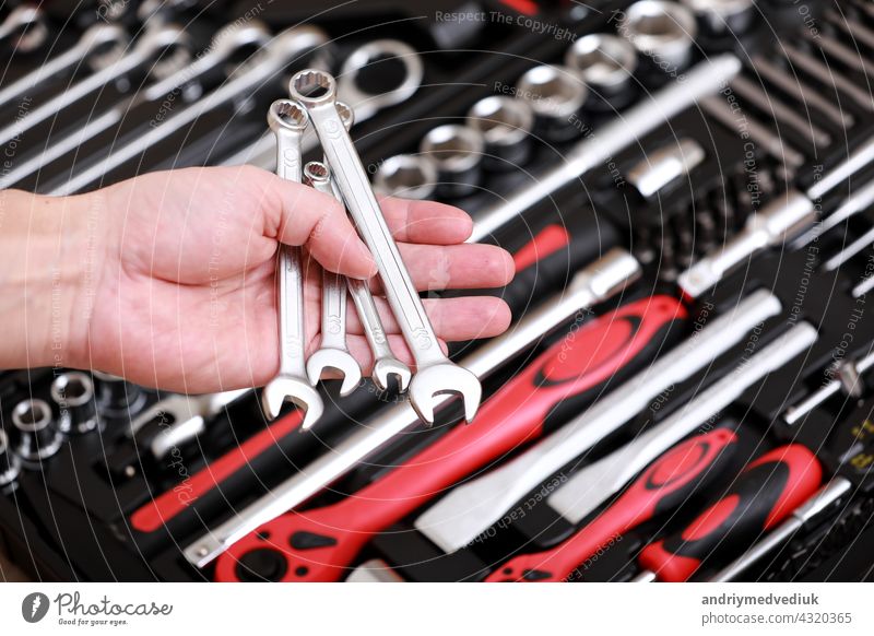 Werkzeuglager. Nahaufnahme einer männlichen Hand, die einen  Schraubenschlüssel hält. Auto-Reparatursatz im Werkzeugkasten.  Reparaturwerkzeugsatz. Im Inneren des Werkzeugkastens befinden sich  schwarz-rote Schraubenschlüssel, Schraubenschlüssel und