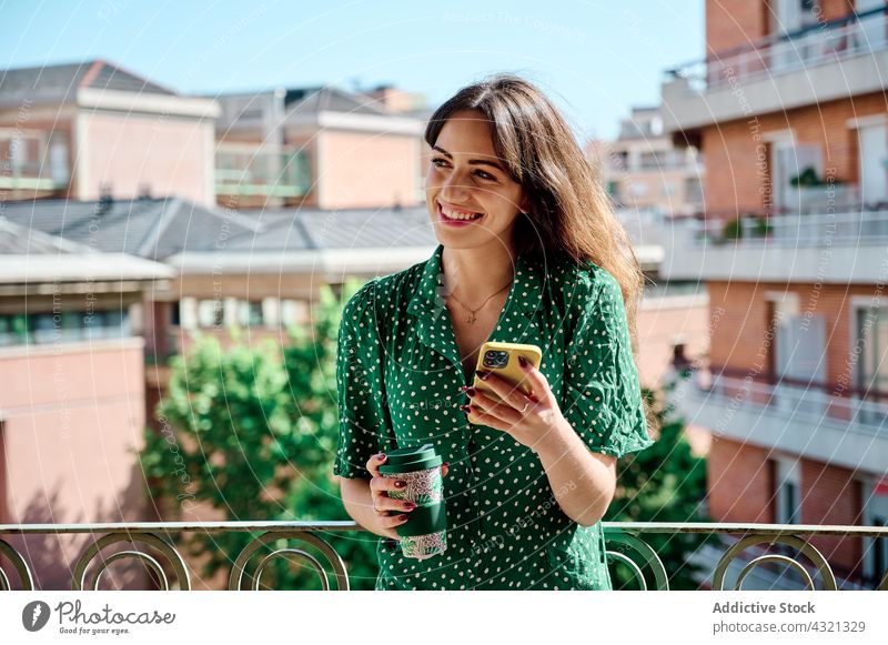 Lächelnde Frau trinkt Kaffee und benutzt ihr Smartphone auf dem Balkon benutzend Mobile Telefon trinken Getränk Sommer Browsen soziale Netzwerke Terrasse