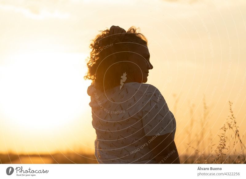 Eine erwachsene Frau genießt die Sonne und ordnet ihr graues Haar mit der Hand während eines Spaziergangs auf einem Feld bei Sonnenuntergang, Spanien