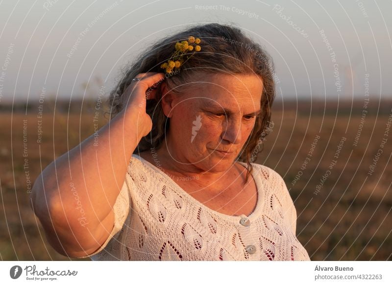 Eine erwachsene Frau schmückt ihr Haar mit einem kleinen Strauß gelber Kamillenblüten, während sie einen Spaziergang auf dem Lande macht, Spanien Erwachsener