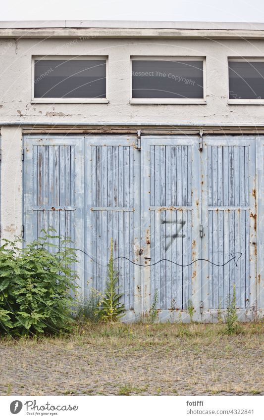 7 | Zahl und Pfeil auf verwittertem Rolltor Tor Holz blau geschlossen Menschenleer Tür Eingang Außenaufnahme zugewachsen Lagerhalle Garage Lagerhaus Halle
