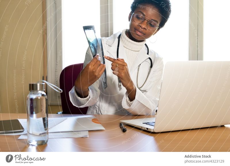 Crop ethnischen Arzt zeigt Röntgenbild gegen Laptop im Büro Sanitäter Bild Stachel Diagnostik schwarz Afroamerikaner analysieren professionell Frau Videoanruf