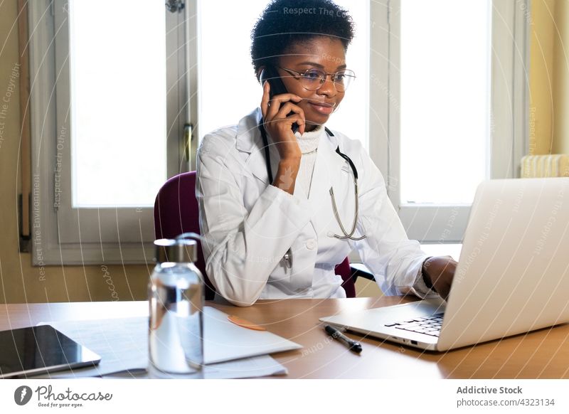 Arzt mit Laptop und Smartphone bei der Arbeit im Büro abgelegen konsultieren benutzend Gesundheitswesen Klinik Sanitäter Praktiker Telefon Frau online Internet