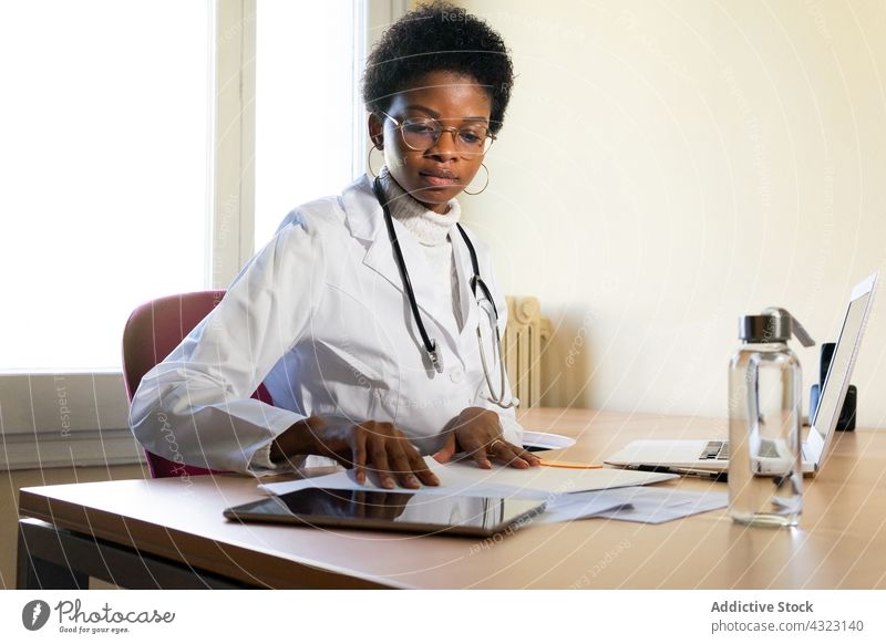 Schwarze Ärztin bei der Arbeit mit Papieren im Büro Arzt Klinik Sanitäter lesen Gesundheitswesen Praktiker Frau Schriftstück jung Afroamerikaner schwarz