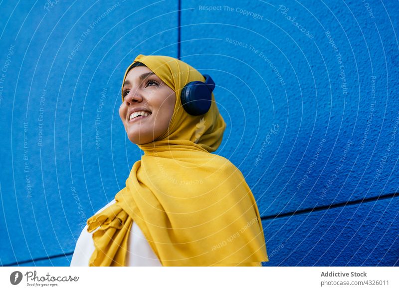 Glückliche muslimische Frau, die mit Kopfhörern Musik hört zuhören Hijab Großstadt ethnisch Gerät Apparatur Kopftuch Gesang Stil Klang urban gelb Kopfschmuck