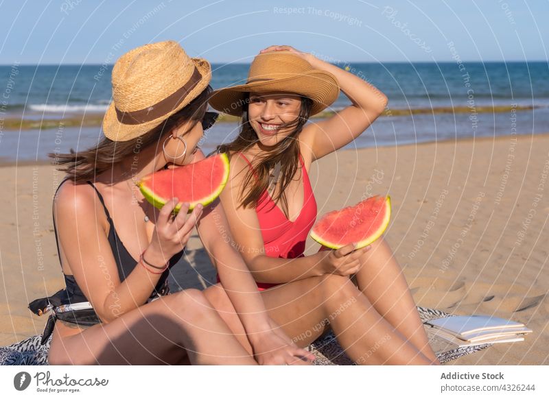 Fröhliche Frau isst Wassermelone am Meeresufer Freund Strand Frauen essen Sommer Badeanzug Urlaub Zusammensein Seeküste Sand Frucht Glück heiter Freundin